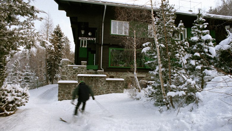 Looshaus im Winter, © Looshaus - Christian Redtenbacher Ein Skifahrer fährt an einem verschneiten Gebäude vorbei, das als Restaurant dient.