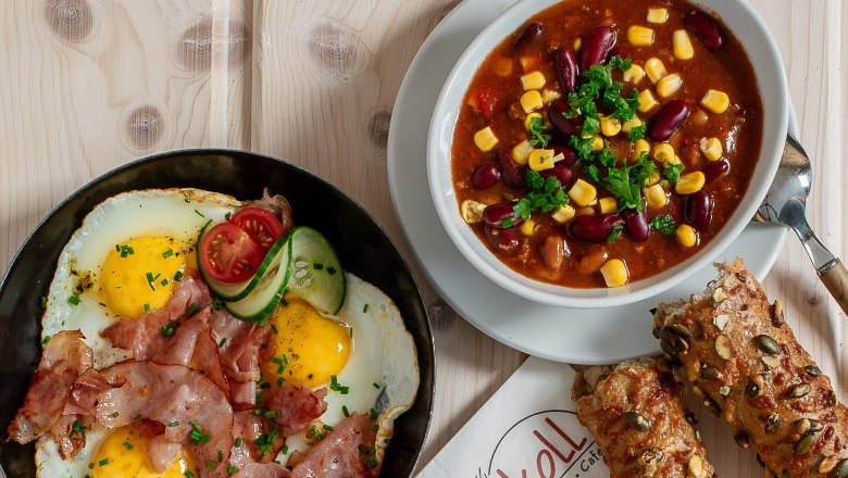 Verschiedene warme Snacks auf einem Tisch, darunter Spiegelei mit Speck, Suppe, belegte Brote und Brötchen.