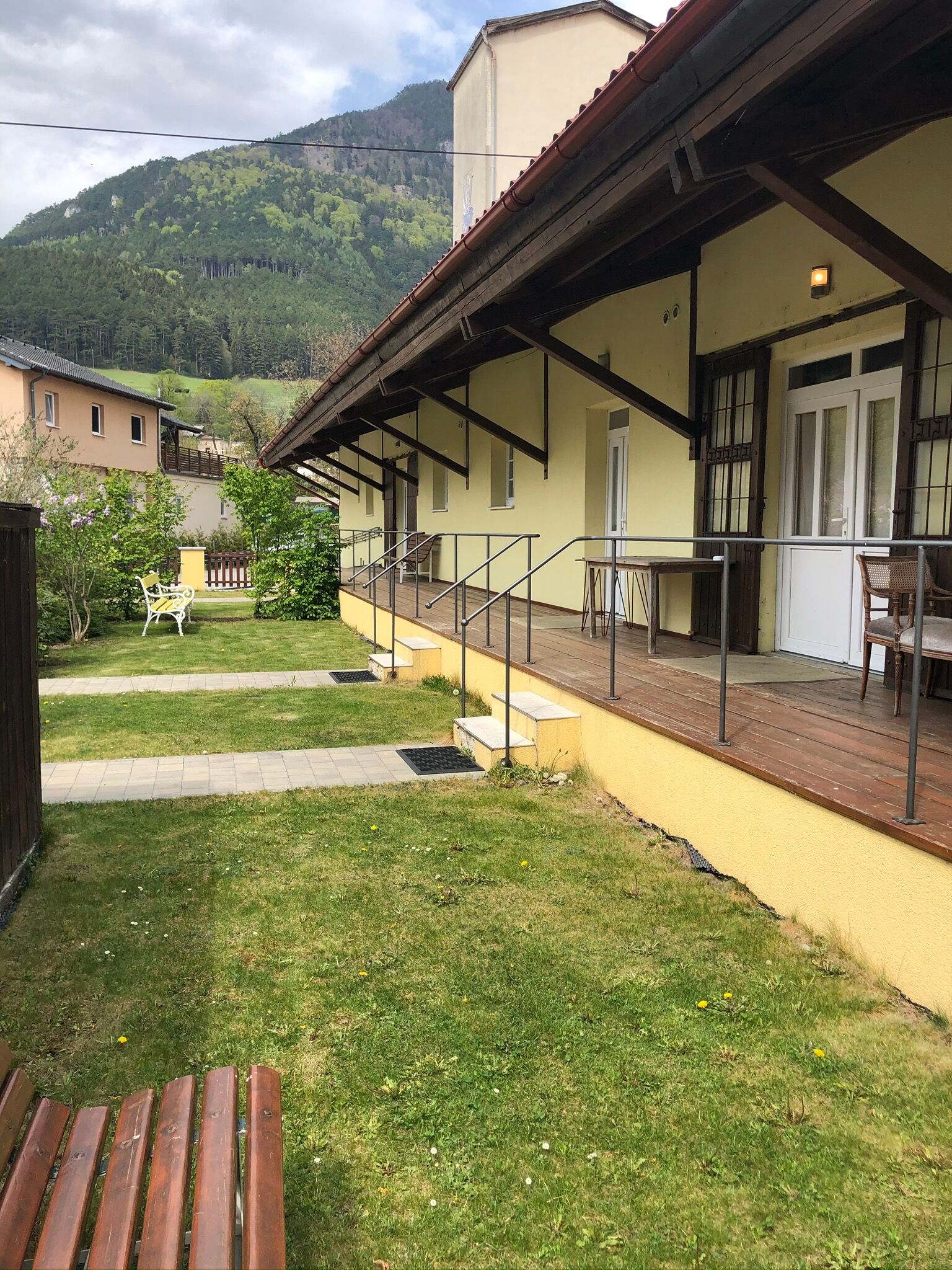 Außenansicht eines gelben Gebäudes mit Veranda und Berg im Hintergrund.