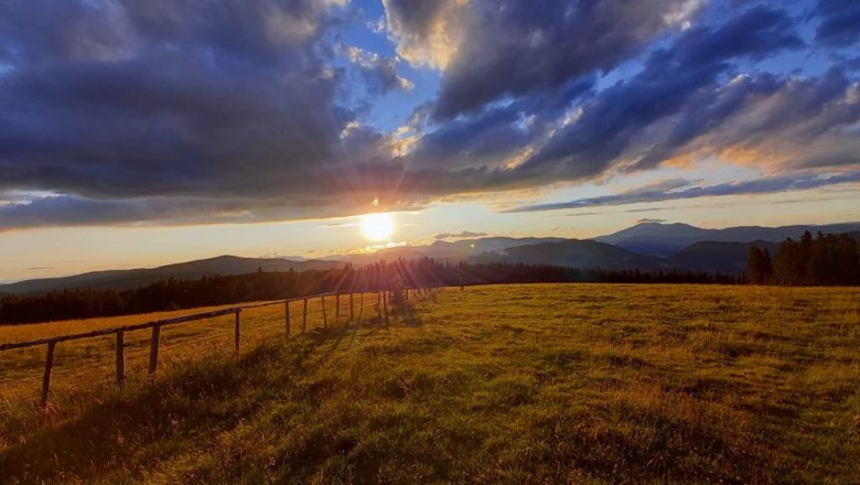 Sunset over a green meadow with mountains in the background and dramatic clouds in the sky.