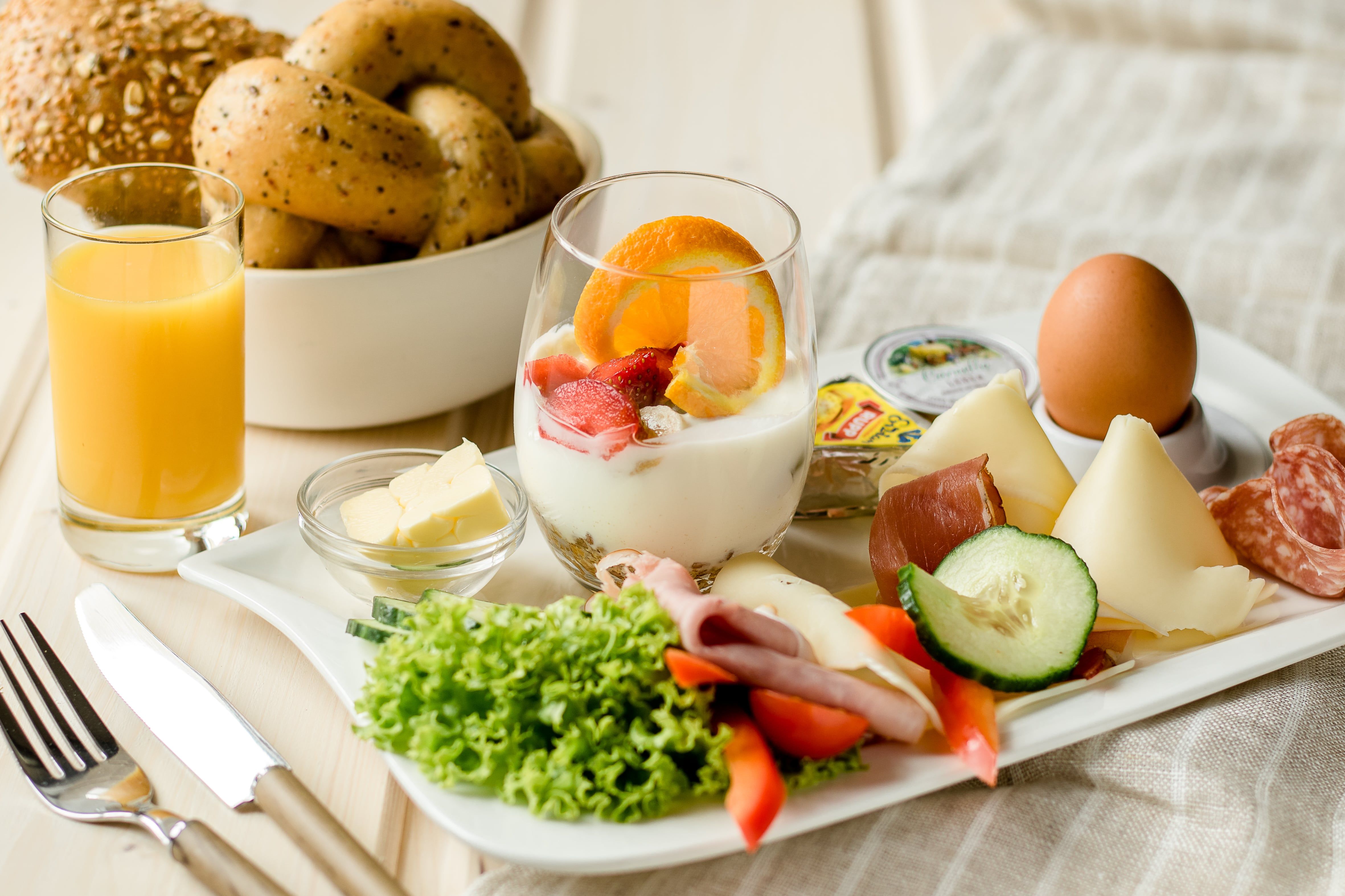 Ein Frühstückstablett mit Joghurt, Obst, Käse, Wurst, Ei, Salat, Butter und Orangensaft.