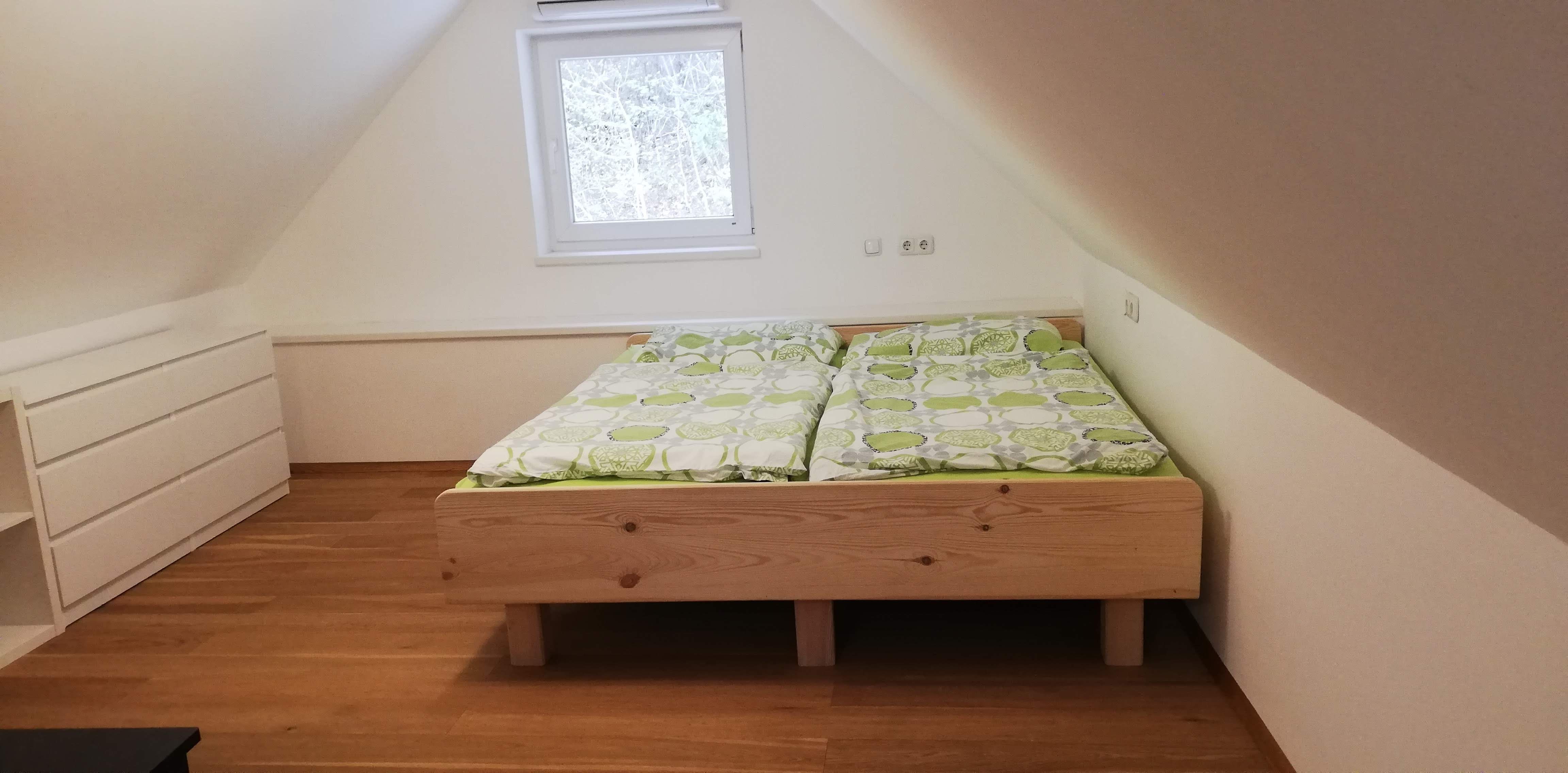 Ein Dachgeschosszimmer mit einem Doppelbett aus Holz und grüner Bettwäsche, daneben eine weiße Kommode.