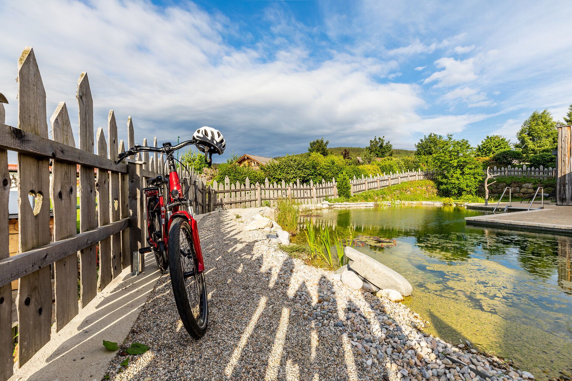 Ein Fahrrad ist neben dem Naturschwimmteich des Sonnenhof Hechtl an den Holzzaun gelehnt.