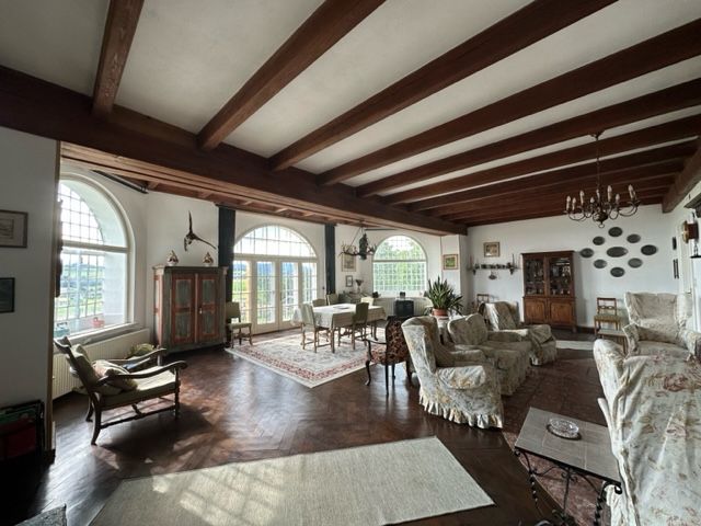 Ein elegantes Wohnzimmer mit antiken Möbeln, Holzbalkendecke, großen Fenstern und Teppichen.