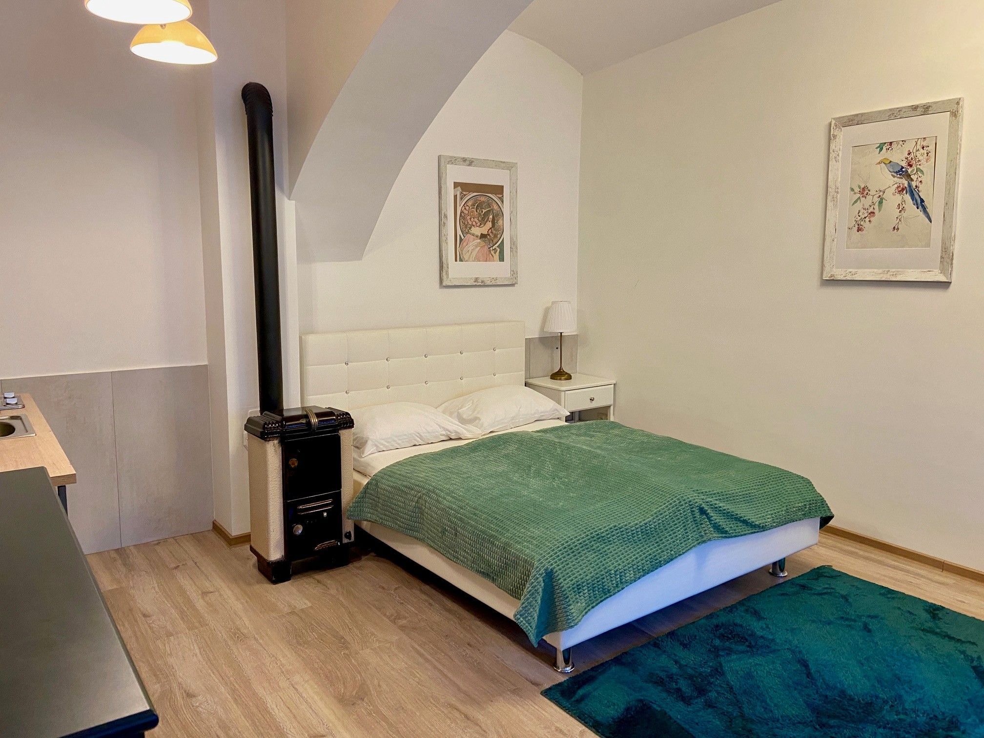 Ein gemütliches Schlafzimmer mit einem weißen Bett, grüner Decke, Teppich und zwei Bildern an der Wand.