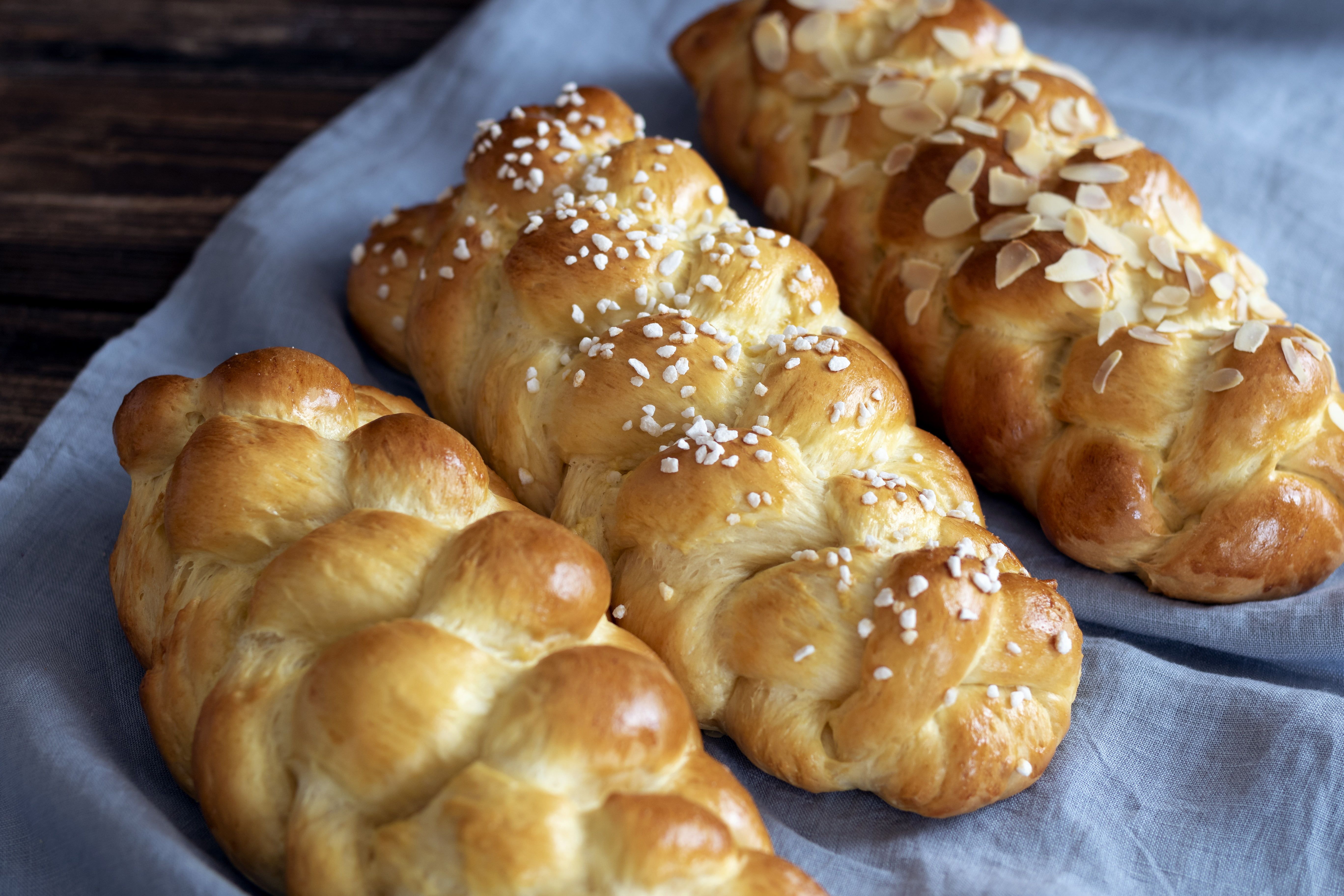 Drei geflochtene Brioche-Striezel auf einem blauen Tuch, einer mit Mandeln, einer mit Hagelzucker bestreut.