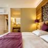 Modern furnished hotel room with double bed, wooden walls and view into the bathroom.