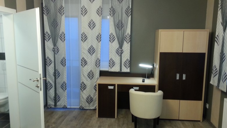 Ein modernes Hotelzimmer mit Schreibtisch, Stuhl und Kleiderschrank.