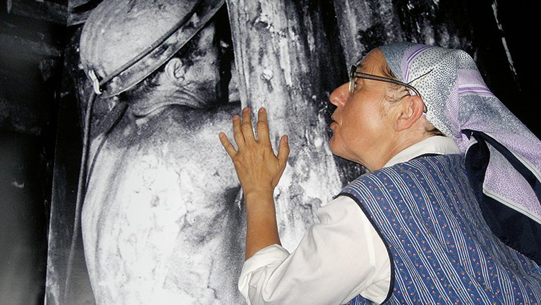 A woman with a headscarf looks at a large black and white photo of a miner.