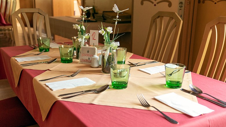 A table laid with yellow and red tablecloths, green glasses and flowers.