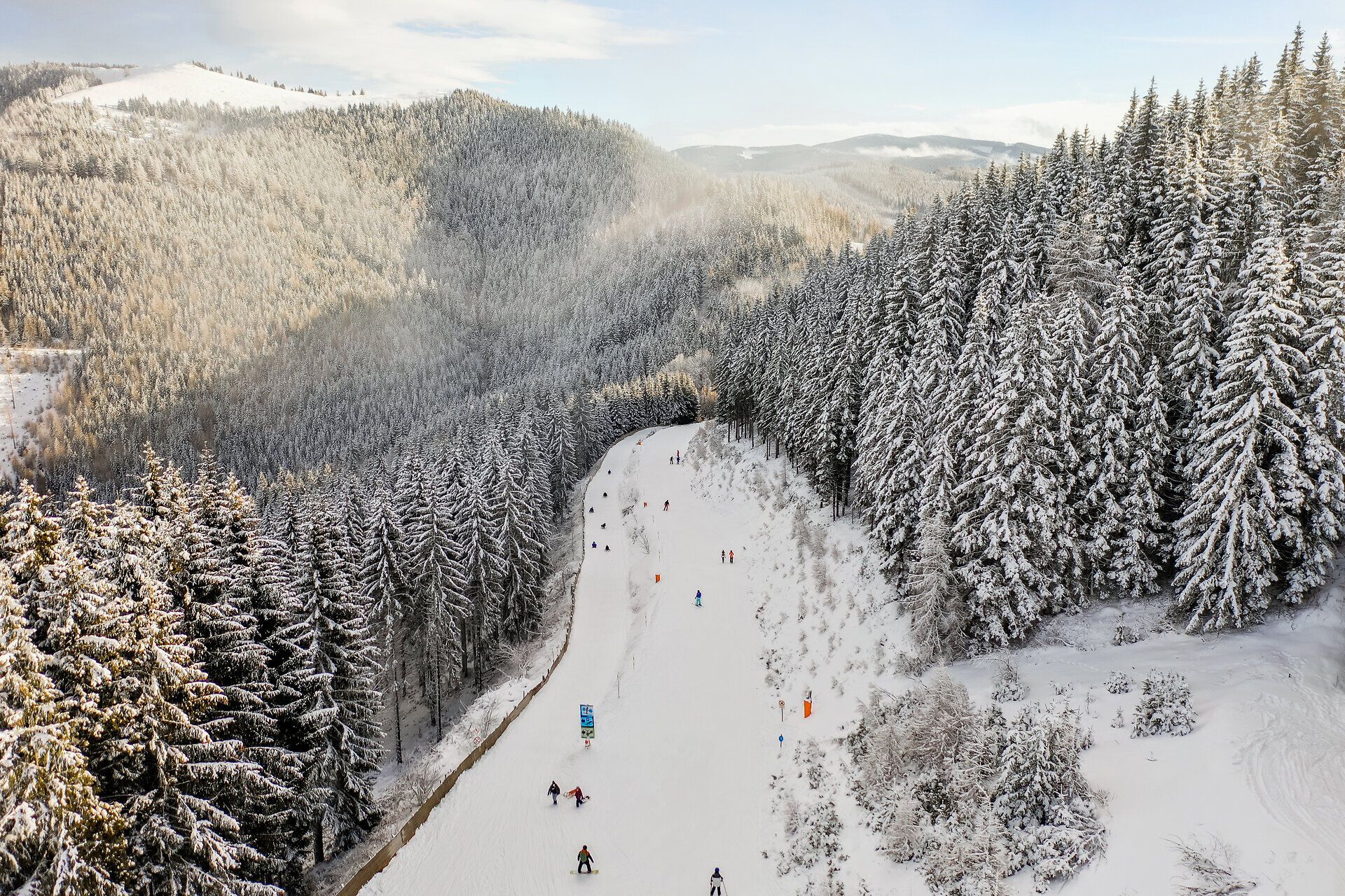 Verschneite Skipiste am Semmering Hirschenkogel, umgeben von dichtem, schneebedecktem Wald.