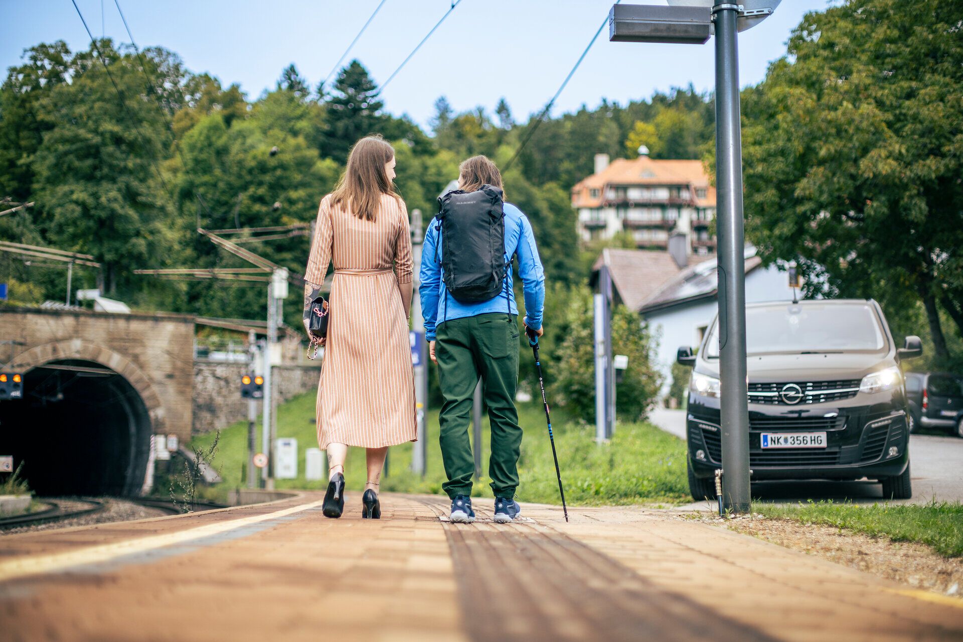 Ein schwarzer Kleinbus, der RUF Bus, holt gerade eine Frau in einem schönen orangen Kleid und einen Wanderer ab. 
