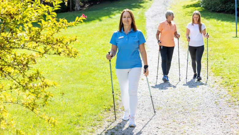 Three people Nordic walking on a gravel path in a green park. One of the people is a trainer from the K&ouml;nigsberg health resort.