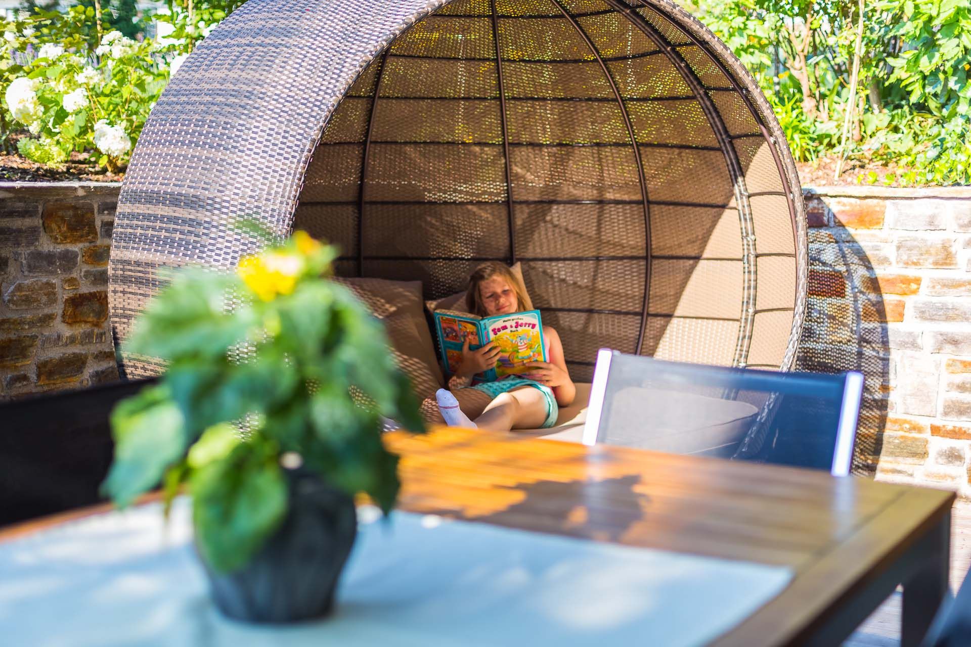 Person liest ein Buch in einer runden, geflochtenen Sitzgelegenheit im Freien.
