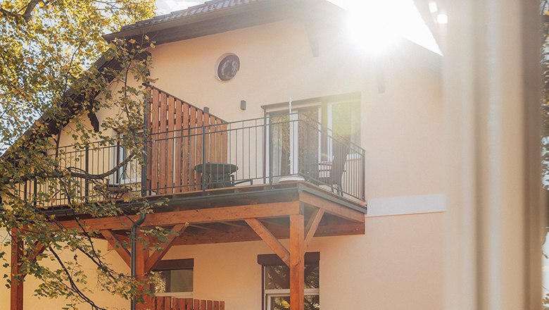 Haus mit Balkon und Sonnenschein durch Bäume.
