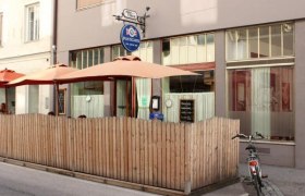 Au&szlig;enansicht eines Caf&eacute;s mit Holzzaun und Sonnenschirmen.