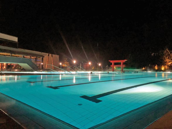 Außenbereich der Linsberg Asia Therme bei Nacht mit beleuchtetem Pool und rotem Torii.