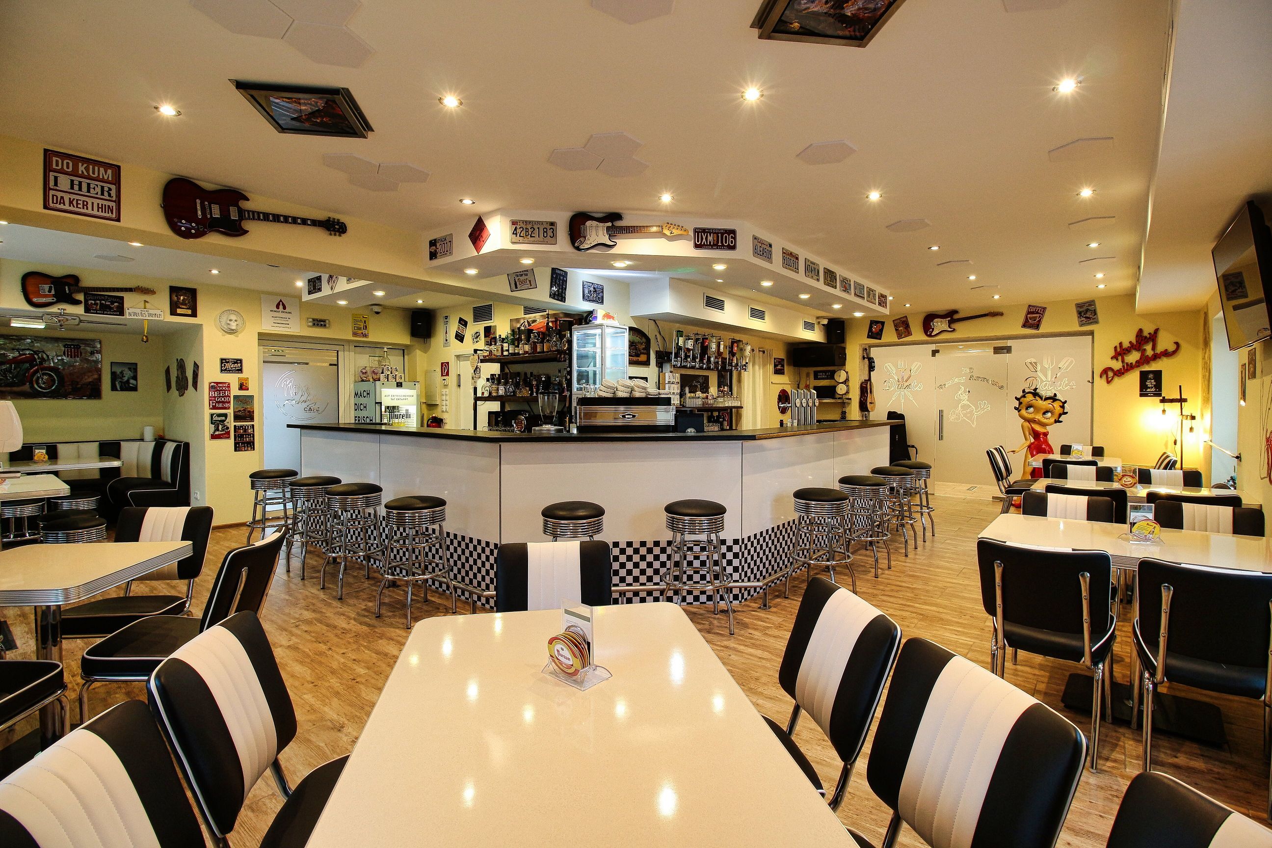 Innenansicht eines Rockabilly-Cafés mit Retro-Dekor, Barhockern und Tischen.