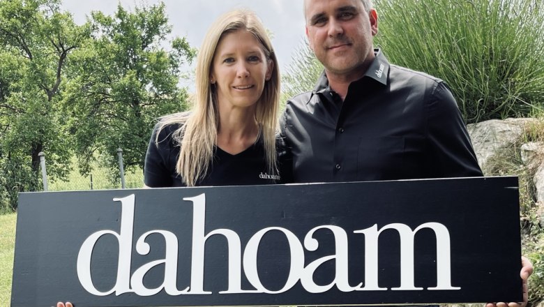 Two people are holding a sign with the inscription 'dahoam' outside.