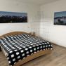 Bedroom with double bed, checkered bedspread, wooden furniture and mountain landscape pictures on the wall.