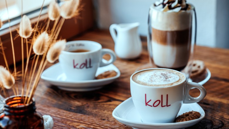 Two cups of coffee on a wooden table, with cookies and a glass of latte macchiato in the background.