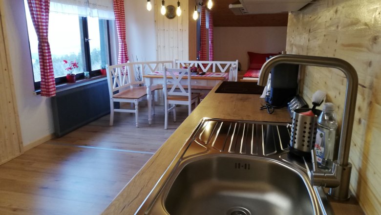 Küche in einem Dachgeschoss-Apartment mit Holzverkleidung, Spüle, Esstisch und roten Vorhängen.