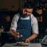 A chef in a striped apron prepares a dish in a kitchen.