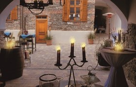 Gemütlicher Innenhof eines Cafés mit Kerzenlicht und rustikaler Steinmauer.