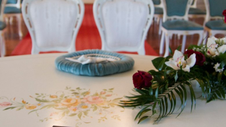 Ein eleganter Raum mit weißen Stühlen und einer Trauungsmappe auf einem Tisch.