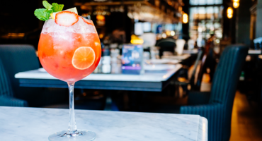 Ein roter Cocktail mit Limettenscheibe und Minze auf einem Marmortisch in einem stilvollen Restaurant.