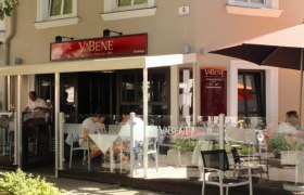 Exterior view of a café called Va Bene with sidewalk seating and guests at tables.
