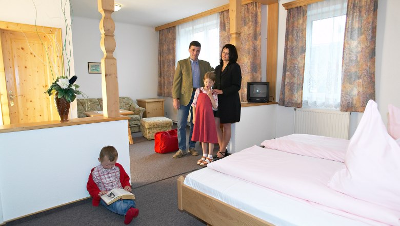 Family in a cozy hotel room with wooden furniture and pink bed linen.