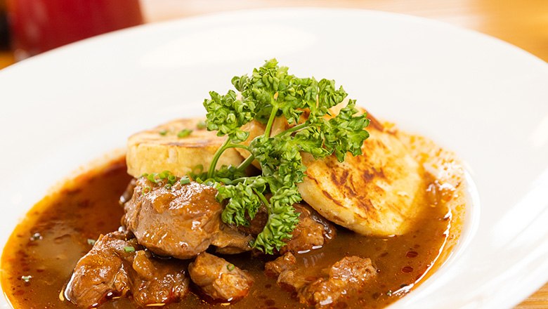 Ein Teller mit Rindsgulsch und Kn&ouml;deln mit Petersilie garniert.