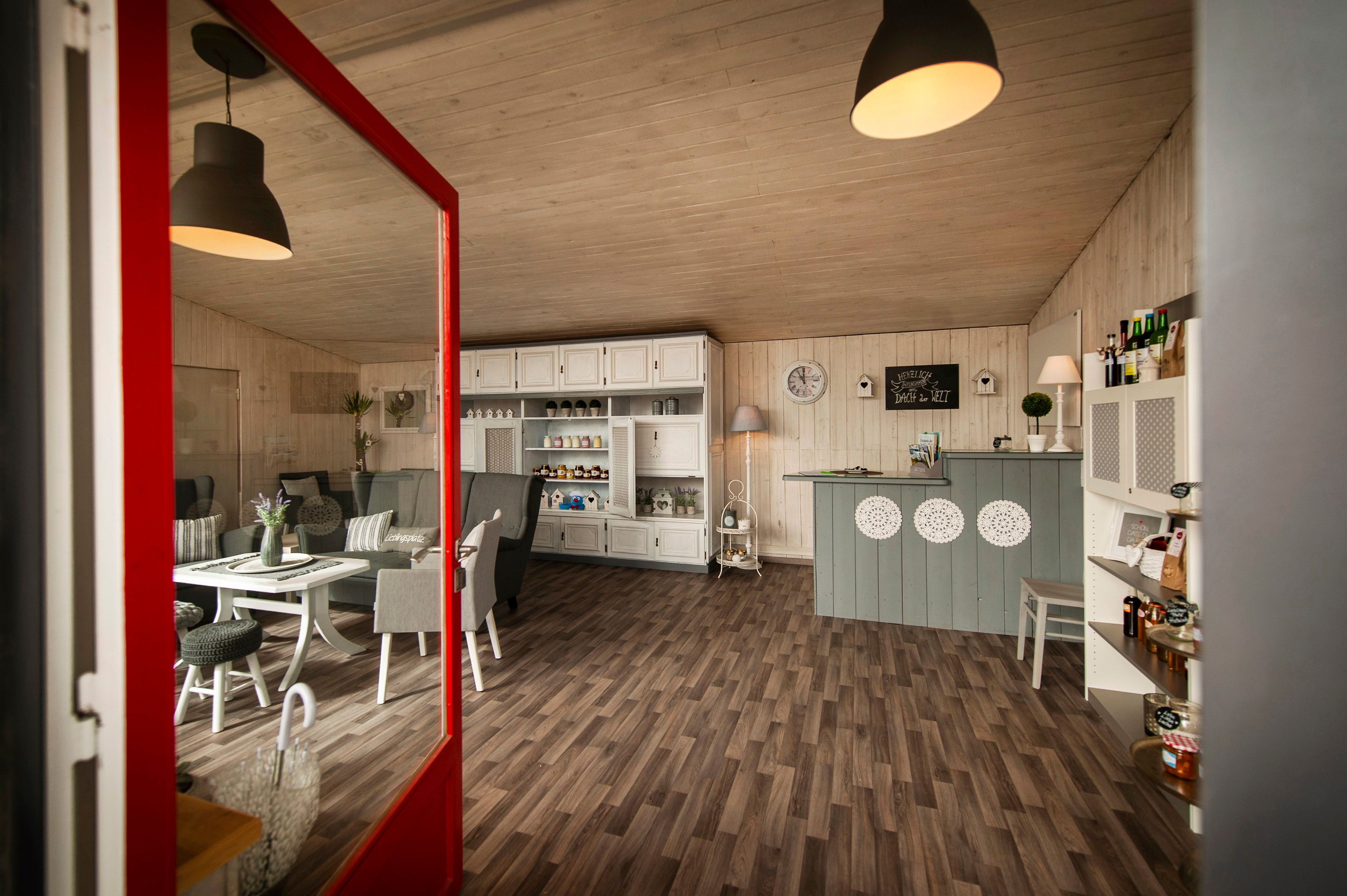 Innenansicht eines gemütlichen Cafés mit Holzboden, weißen Möbeln und dekorativen Elementen.