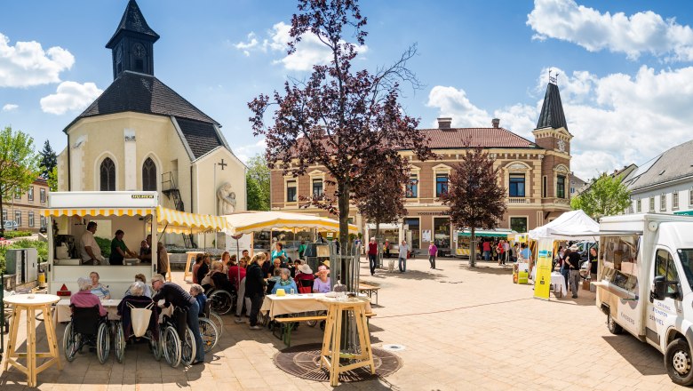 Marktplatz in Gloggnitz mit Kirche, Verkaufsst&auml;nden und Menschen.