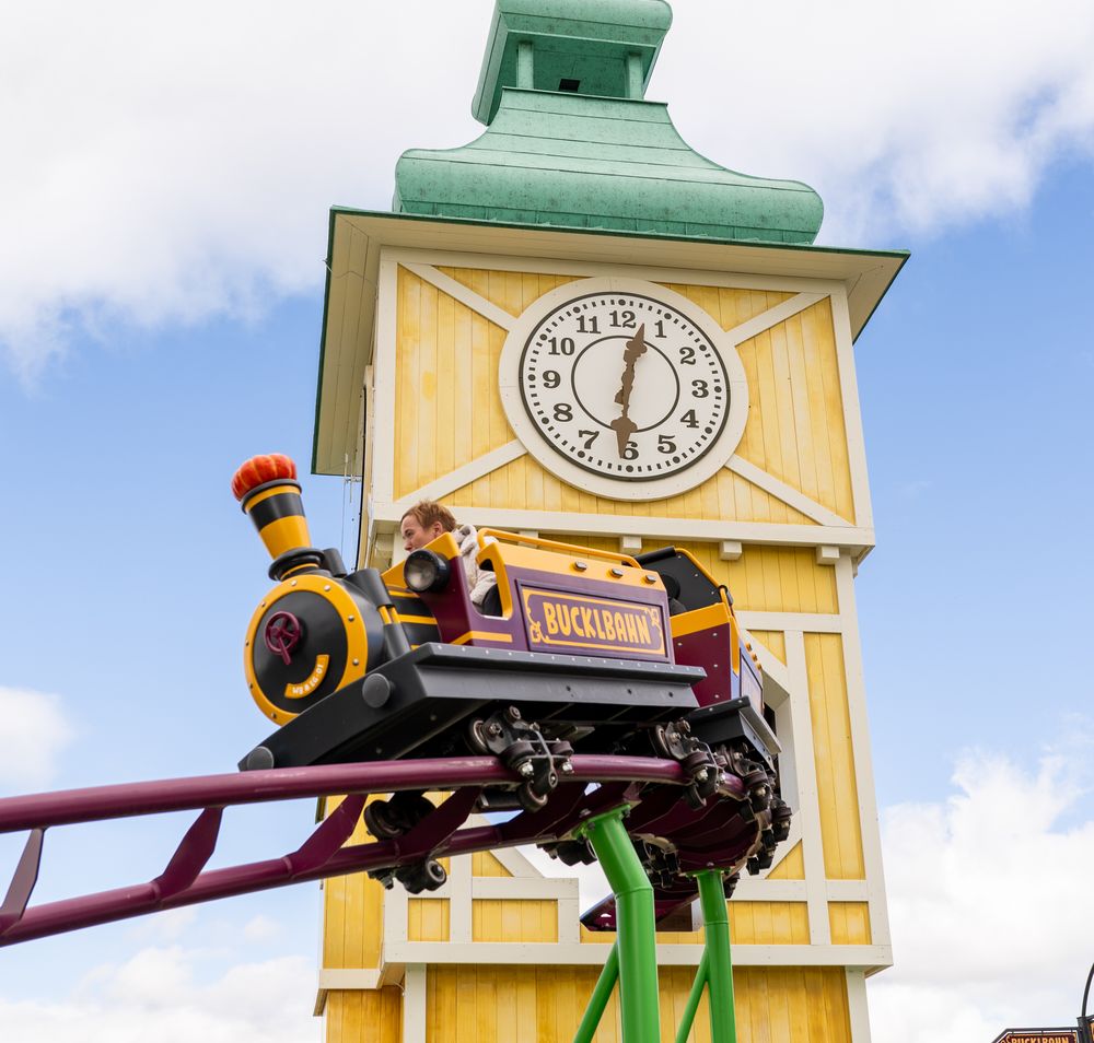 Eine Waggon der Achterbahn Bucklbahn im Eis-Greissler Erlebnispark, im Hintergrund gelber Turm mit Uhr.
