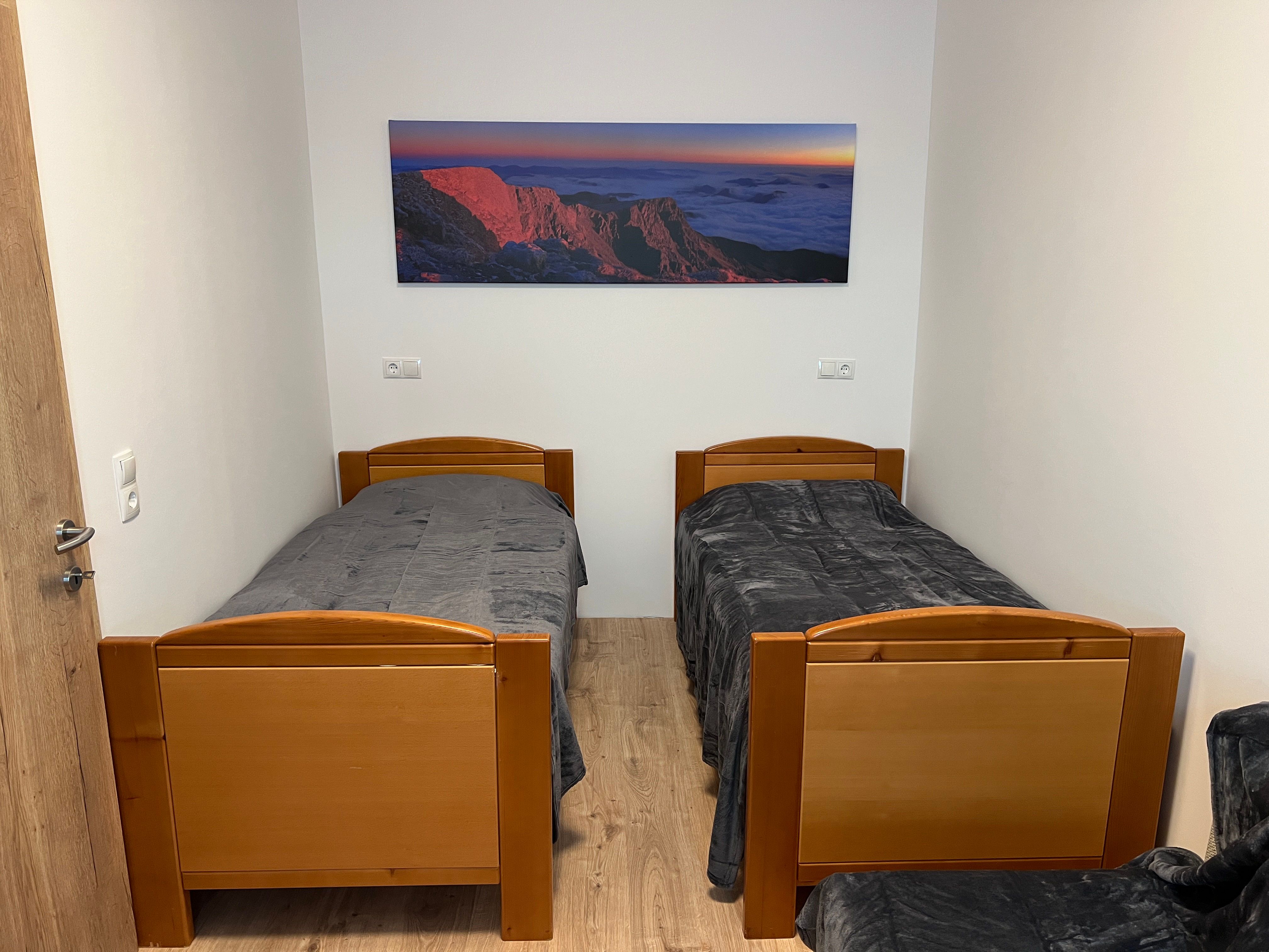 Ein einfach eingerichtetes Zimmer mit zwei Einzelbetten und einem Landschaftsbild an der Wand.
