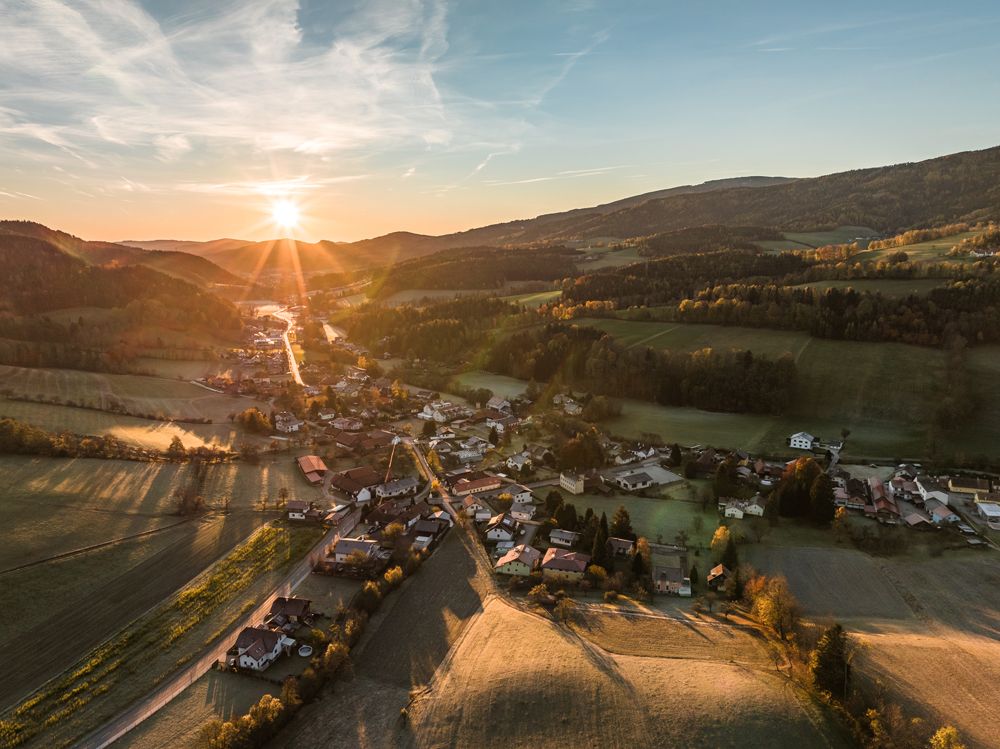 Luftaufnahme eines Dorfes in einer hügeligen Landschaft bei Sonnenuntergang.