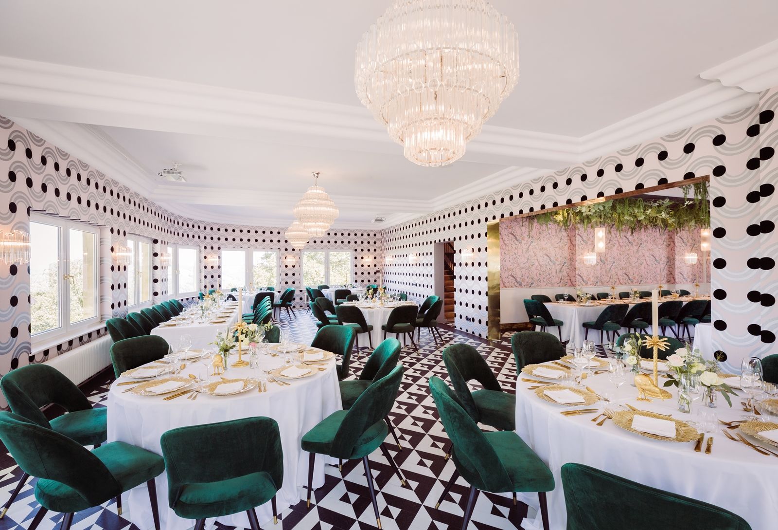 Elegantes Restaurant mit runden Tischen, grünen Stühlen und Kronleuchtern.