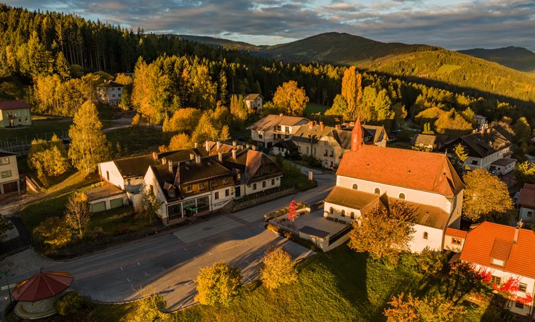 Luftaufnahme von St. Corona am Wechsel mit Kirche und umliegenden Gebäuden in herbstlicher Landschaft.