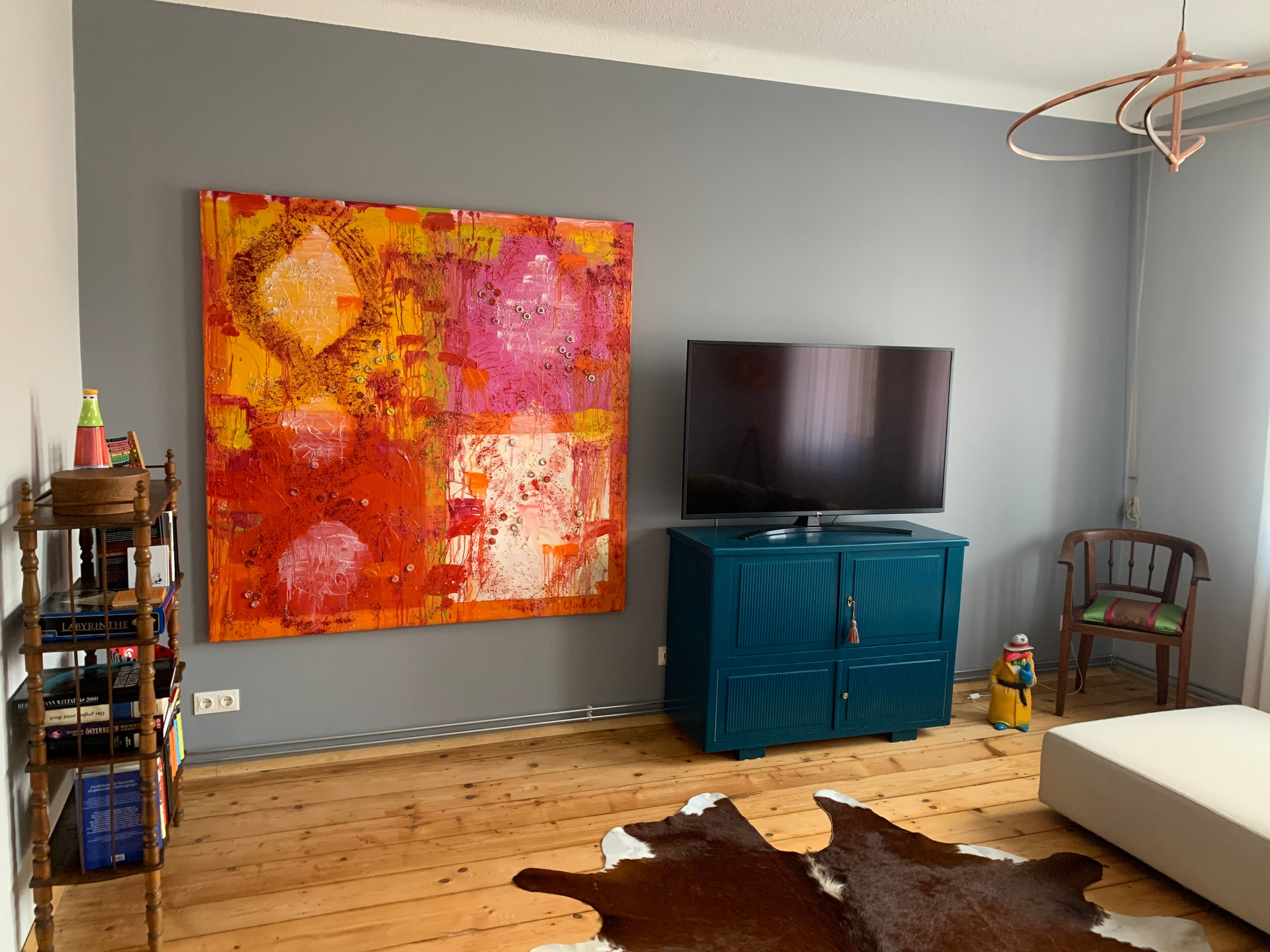 Wohnzimmer mit großem buntem Gemälde, Fernseher auf blauem Schrank, Holzboden und Kuhfell-Teppich.