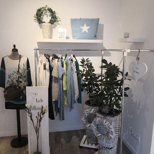 Innenansicht einer Boutique mit Kleidung auf einem Ständer, Dekorationen und Pflanzen.