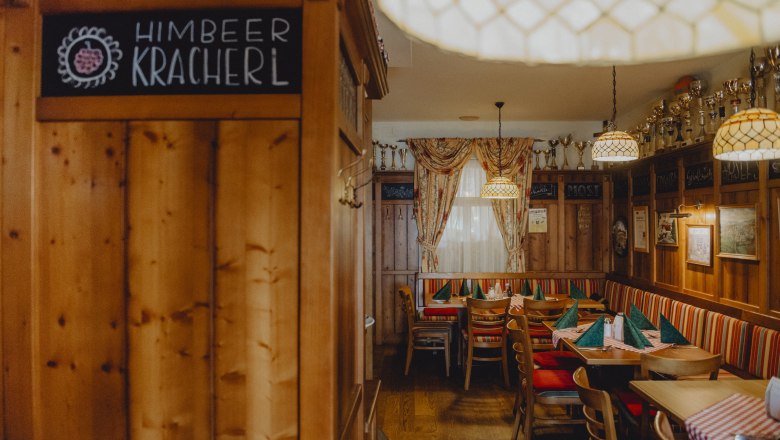 Gemütliche Bauernstube mit Holzmöbeln, karierten Tischdecken und Pokalen auf einem Regal.