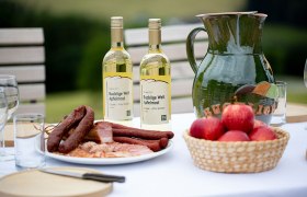 Tisch mit Apfelmost, Wurstplatte, &Auml;pfeln, Holzbrett, Messer und Gl&auml;sern.