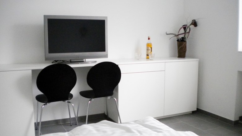 Modernes Zimmer mit Fernseher, zwei schwarzen Stühlen und weißem Schrank.