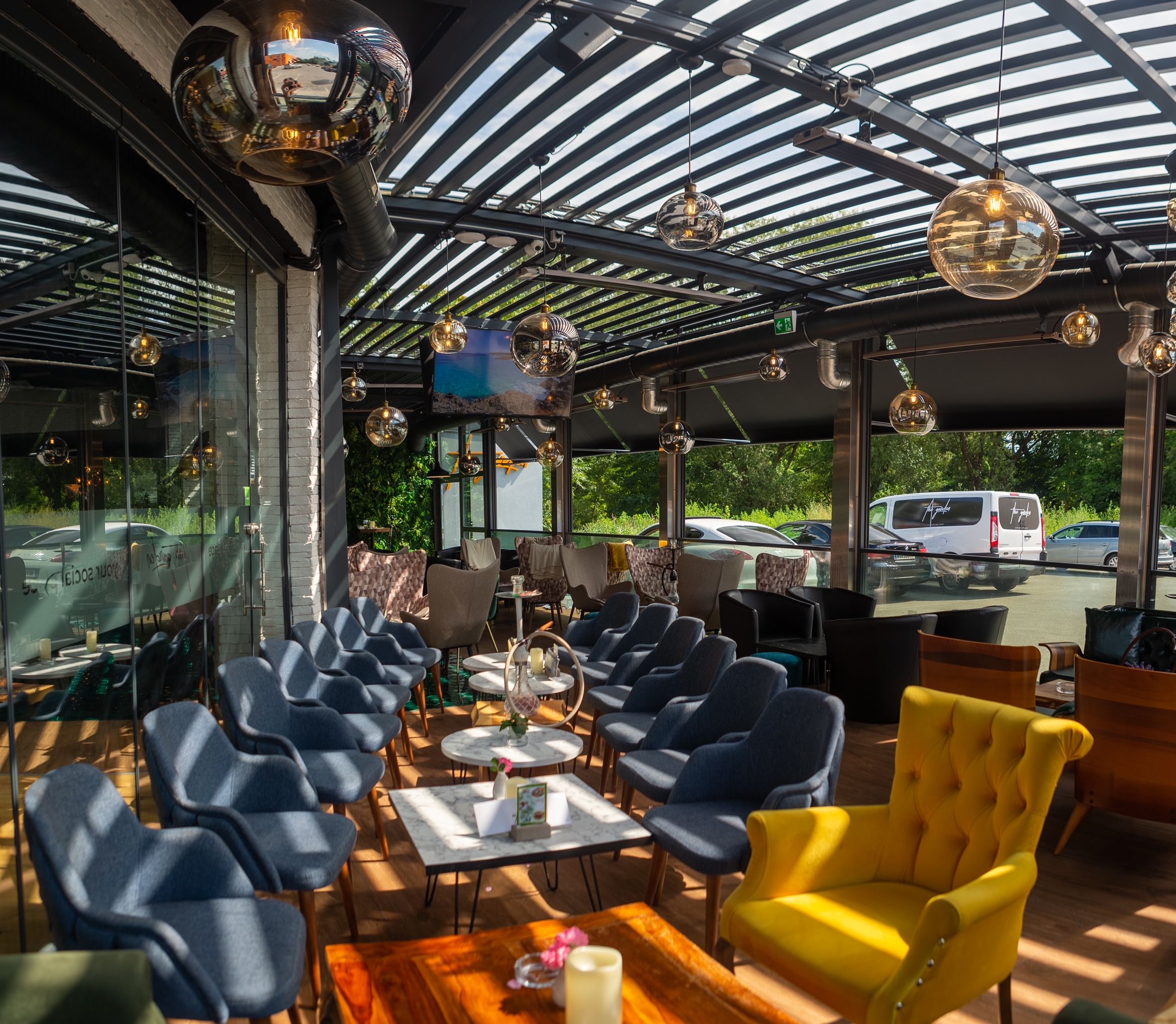 Moderne Terrasse mit blauen und gelben Sesseln, Glaskugelleuchten und Glasdach.