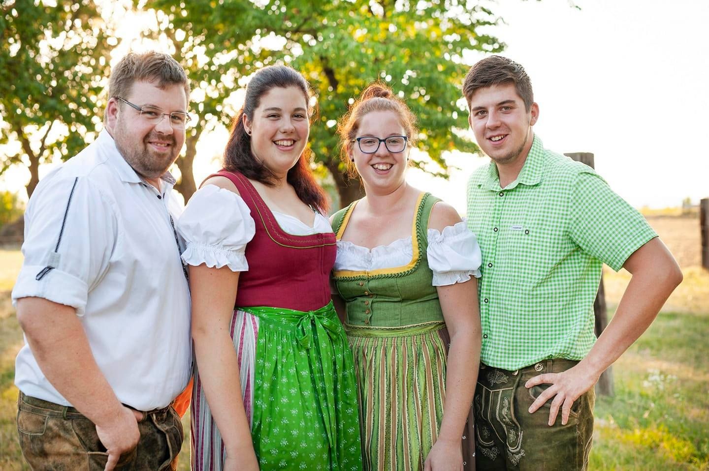 Vier Personen in Tracht stehen auf einer grünen Wiese, im Hintergrund Bäume.