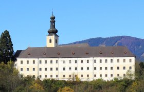Gloggnitz Castle in front of wooded hills and a blue sky.