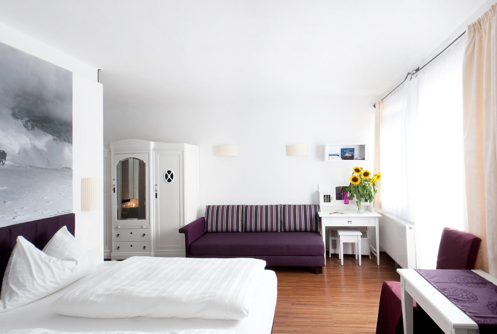 In einem stilvollen Zimmer mit modernem Design und warmen Farbtönen lädt die gemütliche Atmosphäre zum Entspannen ein. Die großen Fenster bieten einen herrlichen Blick auf die umliegenden Berge, während frische Blumen auf dem Tisch eine einladende Note setzen.