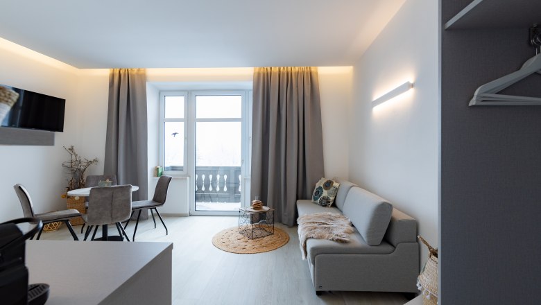 Modernes Wohnzimmer mit grauem Sofa, Esstisch und Balkon.